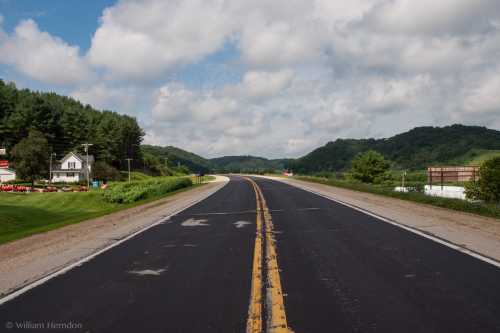 A winding road stretches through green hills under a partly cloudy sky, with a house visible on the side.