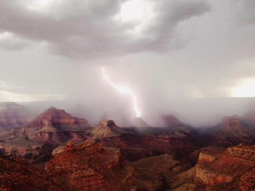 A dramatic view of the Grand Canyon with a lightning strike amidst dark, stormy clouds.