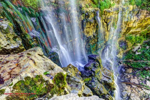 A vibrant waterfall cascading over rocky cliffs, surrounded by lush greenery and colorful moss.