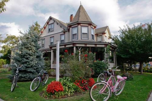 A charming Victorian house with a turret, surrounded by greenery and colorful flowers, with bicycles parked nearby.