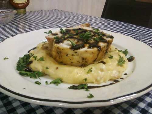 Grilled fish fillet on a bed of creamy mashed potatoes, garnished with fresh herbs, served on a white plate.