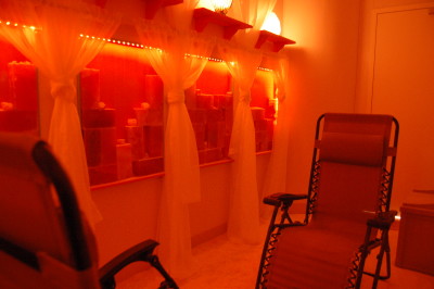 A serene spa room with soft red lighting, featuring shelves of candles and two reclining chairs.