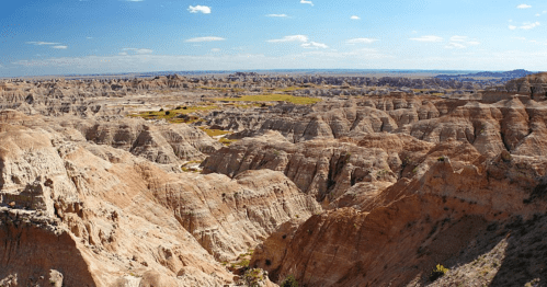 A panoramic view of rugged, colorful rock formations and valleys under a clear blue sky.