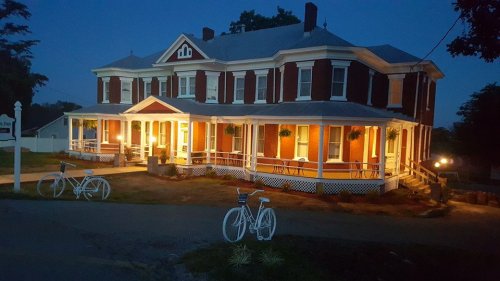 A large, historic house illuminated at night, featuring a wraparound porch and white bicycles in the foreground.