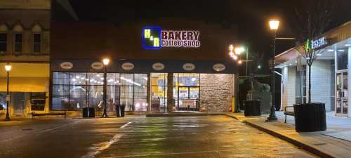 A cozy bakery and coffee shop with large windows, illuminated at night, located on a quiet street.