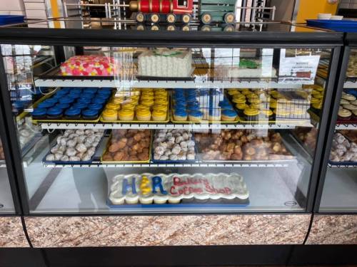 A display case filled with colorful baked goods, including cookies, pastries, and a cake labeled "H&R Bakery Coffee Shop."
