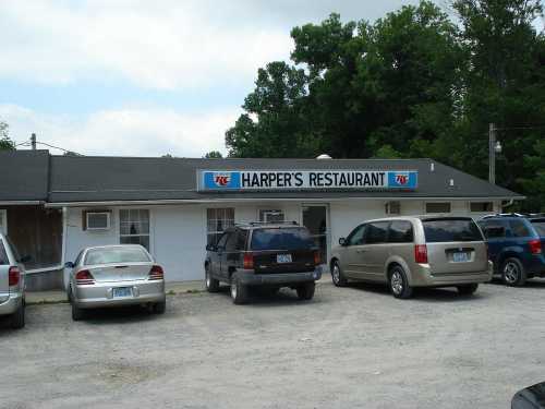 A small restaurant named Harper's with a sign, surrounded by parked cars and trees in the background.