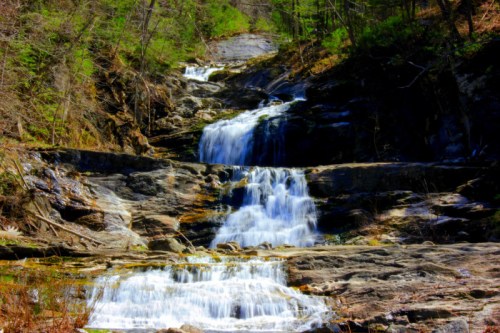 A serene waterfall cascading over rocky terrain, surrounded by lush greenery and sunlight filtering through the trees.