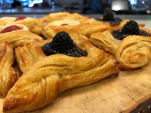 Close-up of flaky pastries topped with blackberries and jam, arranged on a wooden surface.
