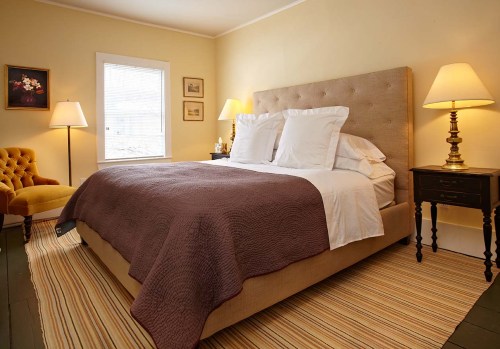 Cozy bedroom with a large bed, yellow walls, a striped rug, and warm lighting from lamps.