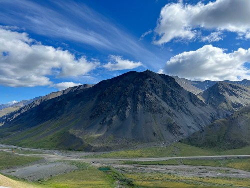 A scenic view of a rugged mountain landscape under a blue sky with scattered clouds and a winding river below.