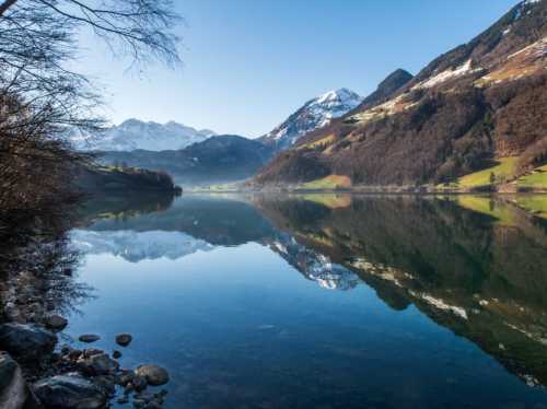 A serene lake surrounded by mountains, reflecting the clear blue sky and snow-capped peaks.