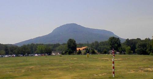 A large, flat-topped mountain rises in the background, surrounded by green trees and a clear blue sky.