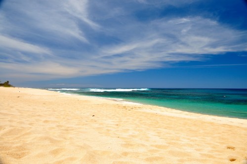 A serene beach with golden sand, gentle waves, and a clear blue sky, creating a tranquil coastal scene.