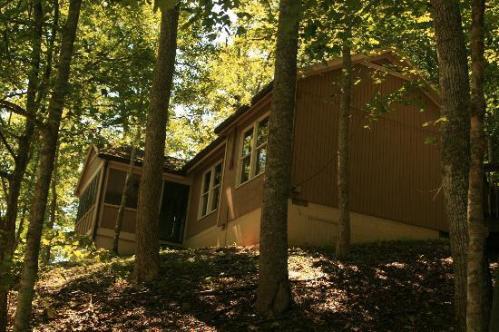 A brown house nestled among trees on a hillside, with sunlight filtering through the leaves.