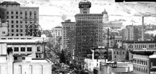 Historic black-and-white cityscape featuring tall buildings and a prominent bank sign in the foreground.