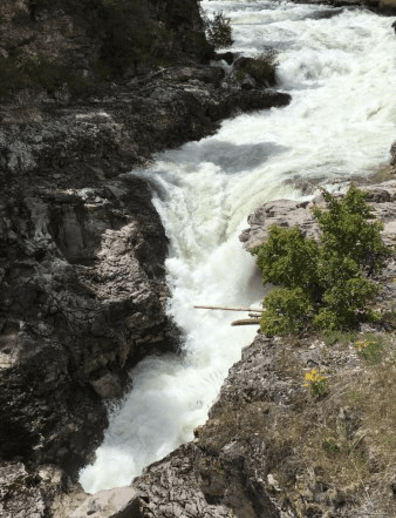 Rushing water cascades over rocky terrain, surrounded by greenery and rugged cliffs.