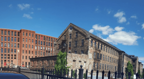Historic brick buildings under a clear blue sky, with a black fence in the foreground.