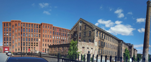 Historic brick buildings under a clear blue sky, with a black fence in the foreground and a chimney on the right.
