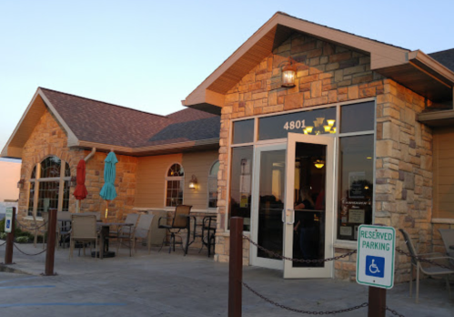 Exterior of a stone and wood building with a welcoming entrance, outdoor seating, and reserved parking sign.