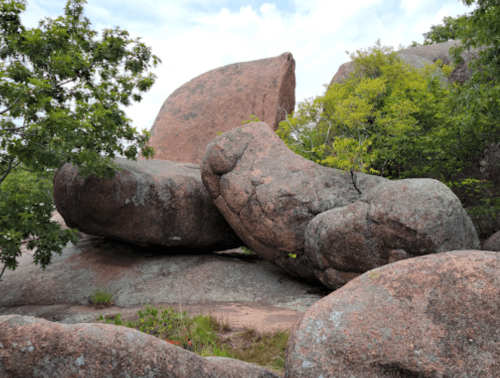 Large, weathered boulders surrounded by greenery under a partly cloudy sky.