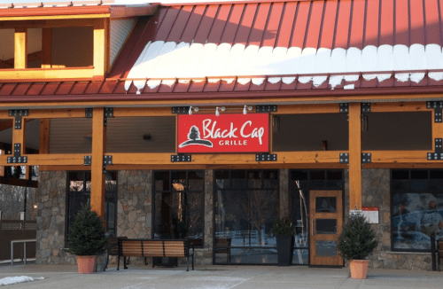 Exterior of Black Cap Grille with a wooden structure, stone accents, and a red roof, featuring a sign above the entrance.