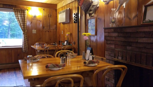 Cozy wooden restaurant interior with tables set for dining, a fireplace, and rustic decor.