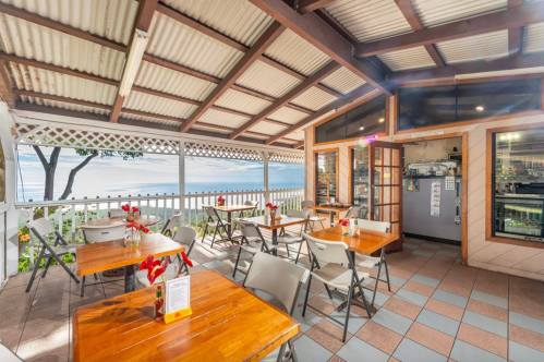 Cozy restaurant interior with wooden tables, chairs, and a view of the ocean through large windows.