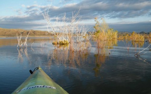 A kayak on calm water surrounded by sparse trees and mountains under a cloudy sky.
