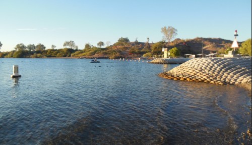 A serene lake scene with gentle waves, surrounded by greenery and a small boat in the distance under a clear sky.