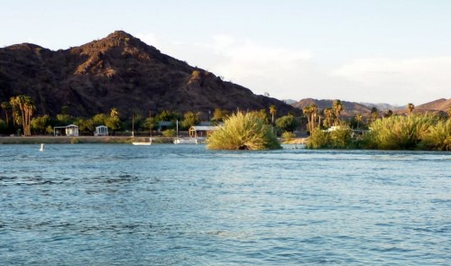 A serene river scene with lush greenery, mountains in the background, and a clear sky.