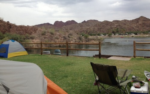 A campsite by a lake with tents, a chair, and mountains in the background under a cloudy sky.