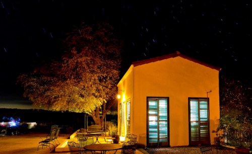 A cozy yellow building at night, illuminated by warm light, with a tree and starry sky in the background.