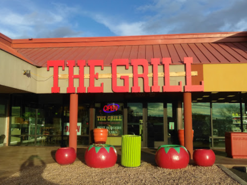 Exterior of a restaurant called "The Grill," featuring colorful tomato-shaped planters and an "Open" sign.