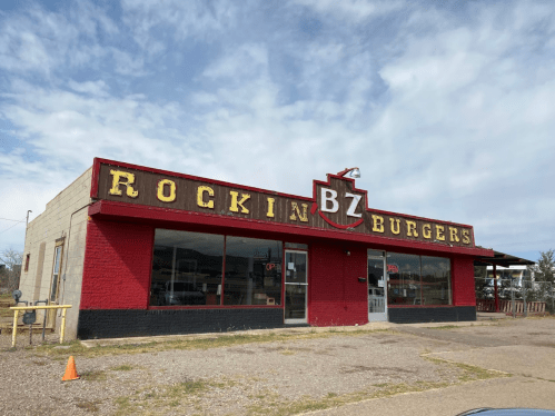 A retro-style burger restaurant with a red and yellow sign reading "Rockin' BZ Burgers" under a cloudy sky.