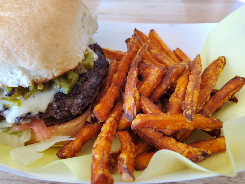 A close-up of a burger with melted cheese and jalapeños, served with a side of crispy sweet potato fries.