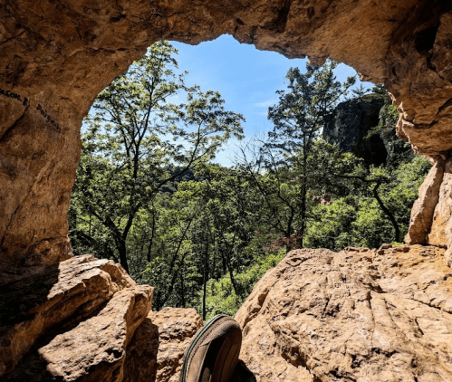 A view through a rocky archway, showcasing lush green trees and a clear blue sky.