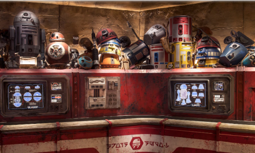 A collection of colorful droid models displayed on a shelf with screens showing droid information in a themed setting.