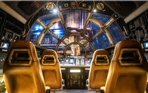 Interior of a futuristic spaceship cockpit with control panels and seats, featuring a large panoramic window.