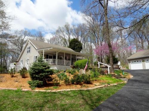 A charming house with a porch, surrounded by greenery and blooming trees, under a partly cloudy sky.