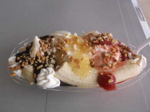 A banana split topped with ice cream, whipped cream, nuts, and various sauces in a clear dish.