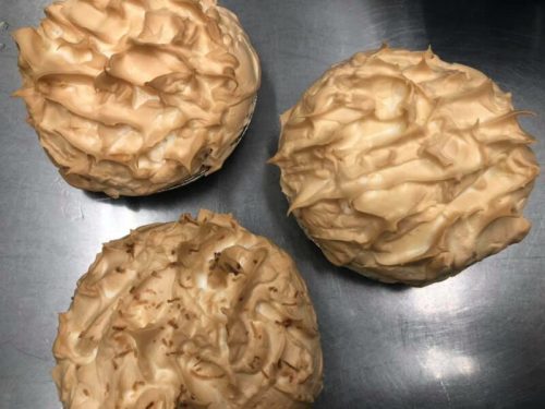 Three pies with fluffy, golden meringue topping on a metal surface. One pie has a light brown topping.