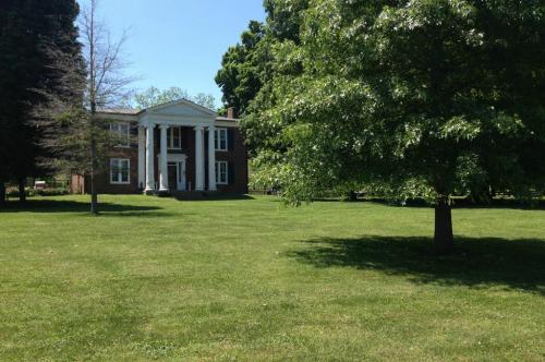 A large brick house with white columns surrounded by green grass and trees on a sunny day.