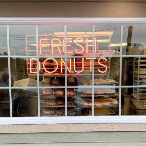 A window display featuring a neon sign that reads "Fresh Donuts" with various donuts visible inside.