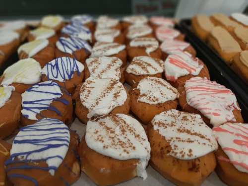 A close-up of assorted donuts topped with colorful icing and whipped cream, arranged neatly on a tray.