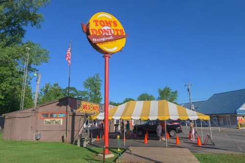 A bright blue sky over Tom's Donuts, featuring a colorful sign and a striped tent outside the shop.