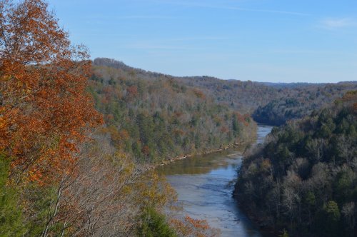 A scenic view of a winding river surrounded by autumn-colored trees and rolling hills under a clear blue sky.