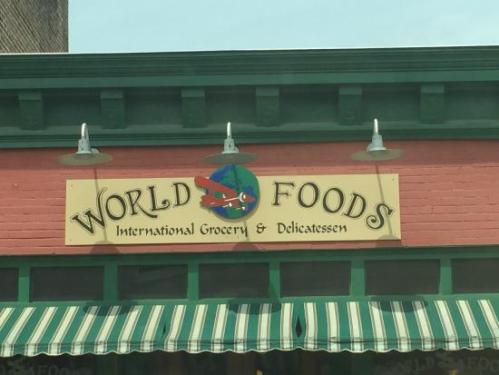 Sign for "World Foods" featuring an international grocery and delicatessen, with a colorful logo and striped awning.