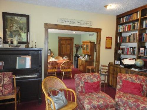 Cozy room with a piano, bookshelves, and seating, leading to a dining area with a round table and chairs.