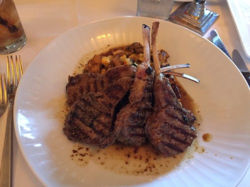 A plate of grilled lamb chops with a savory sauce, served alongside diced vegetables.